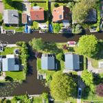 Aerial view of houses along a canal with boats and green areas.