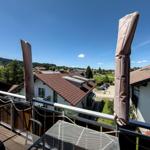 Balcony with table and chairs, view of rooftops and green hills under blue sky.