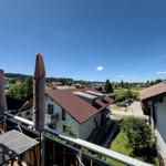 Terrace with table and closed umbrellas. View of roofs, green areas, and mountains under blue sky.