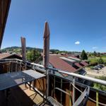 Terrace with table and chairs, view of rooftops and green hills under blue sky.