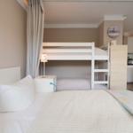 Zimmer mit Doppelbett und Schlafcouch, daneben Doppelstockbett mit Nachttisch und Lampe.