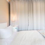 Schlafzimmer mit Bett, Nachttisch und Vorhang. Küche im Hintergrund sichtbar.