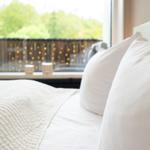 Ein Bett mit weißen Kissen und einer gesteppten Decke vor einem Fenster mit Lichterketten.