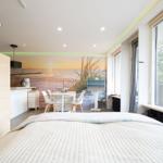 Schlafzimmer mit Blick auf Balkon, Küchenbereich und Wandbild mit Strandmotiv.