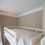 Schlafzimmer mit weißem Hochbett, beige Wände und Nachttischlampe.