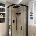 Dusche mit Glaswand, schwarzen Armaturen und Fliesenwand