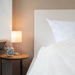 Ein Bett mit weißer Bettwäsche, Nachttisch mit Lampe und Wecker.