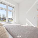 Schlafzimmer mit großem Fenster und Blick auf die Straße. Tür führt in Wohnbereich mit Sofa.