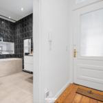 Badezimmer mit schwarzen Fliesen, Badewanne und Toilette. Flur mit Holzboden und weißer Tür.