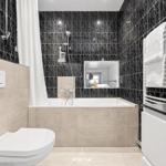 Badezimmer mit Badewanne, Dusche und Toilette. Schwarze Marmorfliesen und weiße sanitäre Einrichtung.