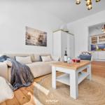 Wohnzimmer mit Sofa, Tisch und Küchenbereich im Hintergrund.