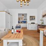 Wohnzimmer mit Holztisch, Sofa und Küchenbereich im Hintergrund.