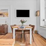 Esszimmer mit Holztisch, Stühlen und Fensterblick. Wandbild und Fernseher an der Wand.