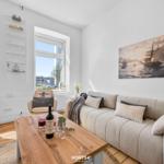 Wohnzimmer mit Sofa, Holztisch und Fensterblick auf die Straße.