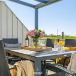 Terrace with table, chairs, and floral arrangement. Background: green field and clear view.