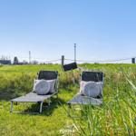 Two lounge chairs with cushions on a green lawn under a blue sky.