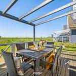 Terrace with table and chairs under glass roof. View of green grass and holiday home.