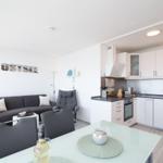 Living kitchen with sofa, dining table, and kitchen cabinets. Wall with OSTSEE sign.