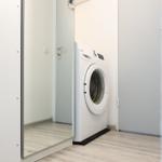 Washing machine in a room with wooden floor and mirrored wall.