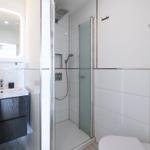 Bath with shower, sink, and toilet. Modern setup with glass partition and lit mirror.