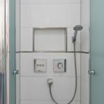 Shower with showerhead, controls, and built-in shelf on white tiled walls.