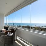 Balcony with table and chairs overlooking the sea through large glass windows.