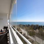Terrace with table and chairs offers view of sea and trees.