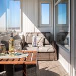 Terrasse mit Sitzgruppe, Tisch und Getränken. Glaswand und Fenster bieten Aussicht.