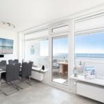 Essbereich mit TV und Blick aufs Meer über große Fenster.
