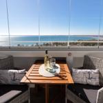 Terrasse mit Tisch und zwei Stühlen, Blick auf Meer und Strand.