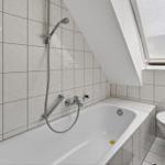 Bathroom with bathtub, shower, and toilet under sloped ceilings.