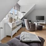 Living room with sloped ceiling, sofa, TV, and wooden floor.