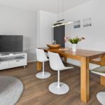 Living and dining area with wooden table, white chairs, TV, and flowers.