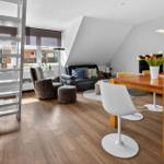 Living and dining area with wooden floor, table, chairs, and staircase.