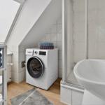 Bathroom with washing machine, sink, and shower under sloped ceiling.