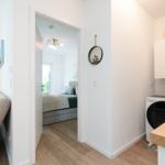 Living area with bedroom and washing machine. Wooden floor and white walls.