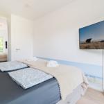 Bedroom with bed, TV, and window. Wall with beach motif.