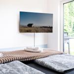 Bedroom with bed, towels, and TV on wall. Doorway to terrace with view of green areas.