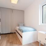 A bedroom with single bed, wardrobe, and nightstand. Window and wooden floor.