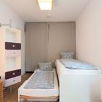 Room with two beds, wardrobe, and window. Bedding in gray.