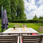 Terrace with table, chairs, and sunshade. Lawn and hedge in the background.