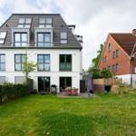Modern villa with garden, terrace, and grill area. Next to a red brick house.
