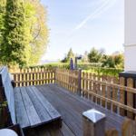 Wooden terrace with benches and fence, view of green garden and sky.