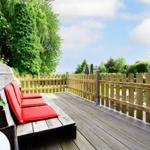 Wooden terrace with red bench and fence. Green trees and sky in the background.