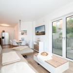 Living room with sofa, coffee table, and TV. Access to kitchen and terrace.