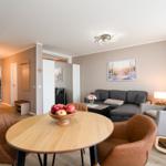 Living and dining area with sofa, chairs, and table. Wall art and lighting visible.