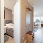 Bedroom with bed and nightstand. Hallway to living and dining area with table, chairs, and balcony.