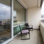 Balcony with two chairs and a small table. Glass doors lead into the apartment.