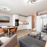 Apartment with kitchen, dining area, and living room. TV, table, sofa, and flowers.