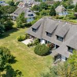 Dorfhaus mit Strohdach, großem Garten und Terrasse. Umgeben von Bäumen und weiteren Häusern.